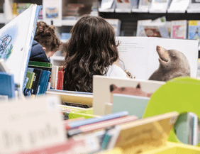 Zwei Kinder lesen in einer Bibliothek, umgeben von Kinderbüchern.