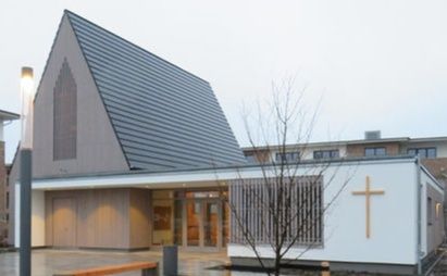 Moderne Kirche mit spitzem Dach und Kreuz an der Fassade.