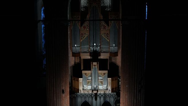 Eine beleuchtete Orgel in einer dunklen Kirche, umgeben von gotischen Bögen.