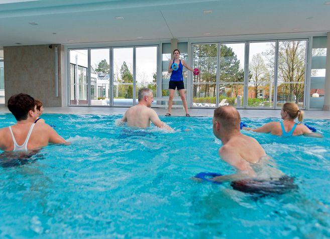 Gruppe von Senioren bei Wassergymnastik in einem Hallenbad mit Trainerin.