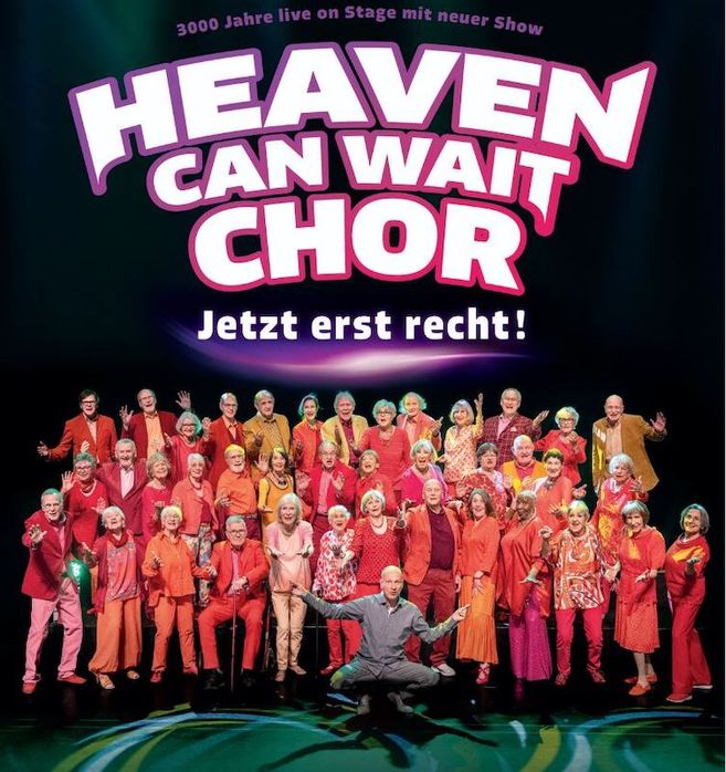 Eine Gruppe älterer Menschen in bunten Outfits posiert auf einer Bühne unter dem Schriftzug 'Heaven Can Wait Chor - Jetzt erst recht!'