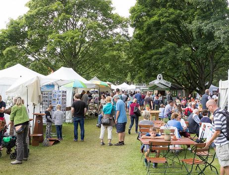 Menschen auf einem Kunsthandwerkermarkt mit Ständen und Sitzgelegenheiten im Freien.