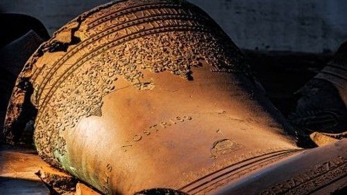 Große, liegende Glocke mit Verzierungen und Inschrift in Nahaufnahme.