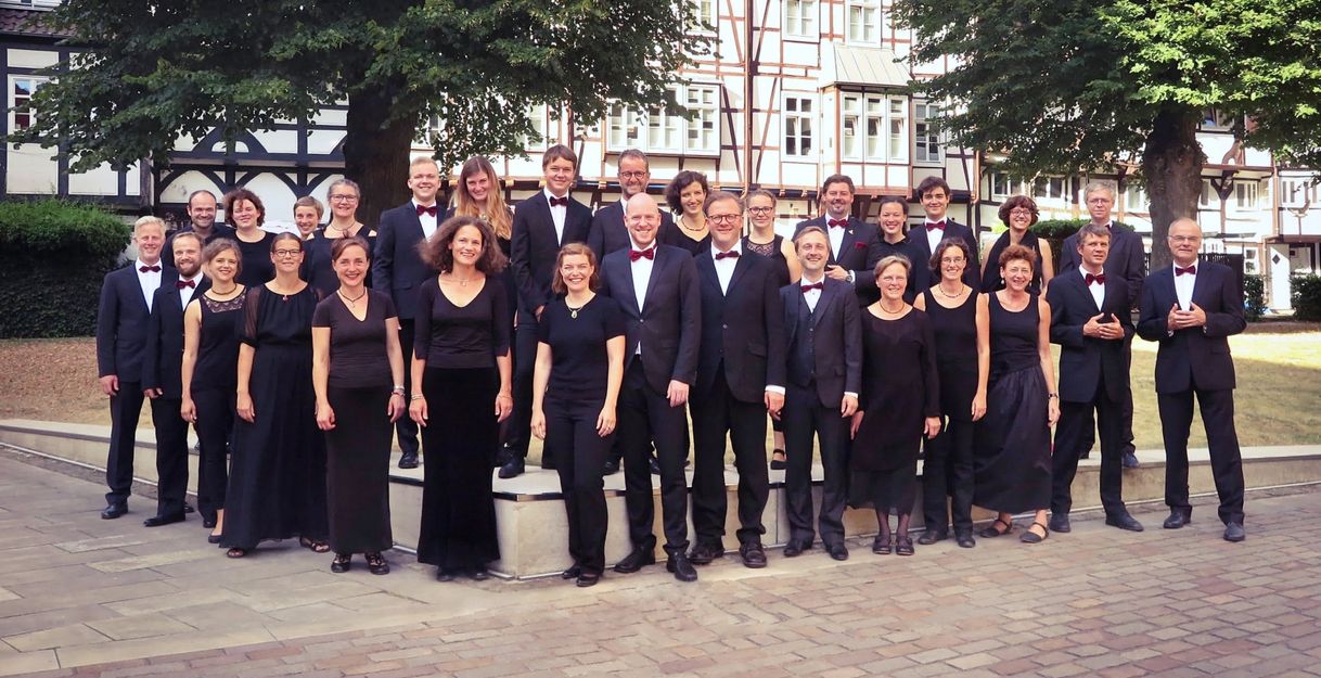 Eine Gruppe von Menschen in eleganter Kleidung posiert draußen vor Fachwerkhäusern.
