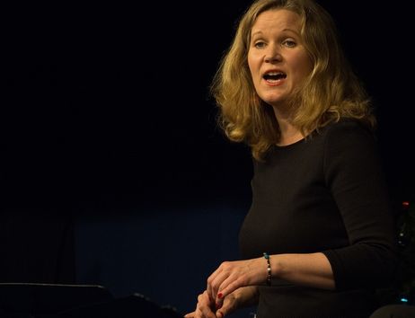 Eine Frau singt auf einer Bühne in einem dunklen Raum.