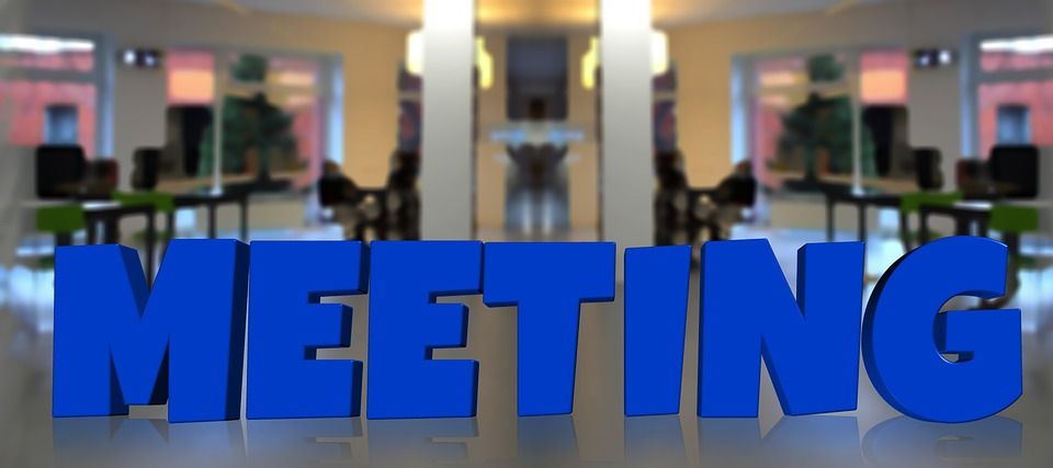 Großer blauer Schriftzug 'MEETING' vor einem unscharfen Bürohintergrund.