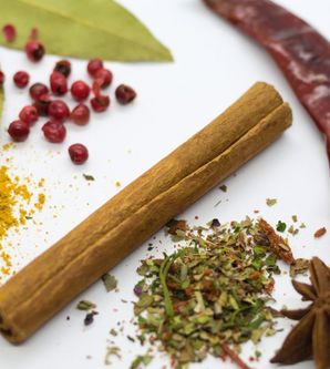 Verschiedene Gewürze auf weißem Hintergrund, darunter Zimtstange, Lorbeerblätter, rote Beeren, getrocknete Chilischoten und Sternanis.