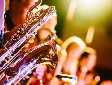 Nahaufnahme eines Saxophons, das von einer Person in einem Konzert gespielt wird, mit verschwommenem Hintergrund und warmem Licht.
