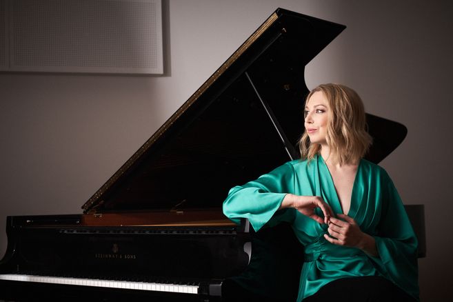 Eine Frau in einem grünen Kleid sitzt neben einem Flügel.