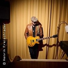 Ein Mann mit Gitarre steht vor einem gelben Vorhang.