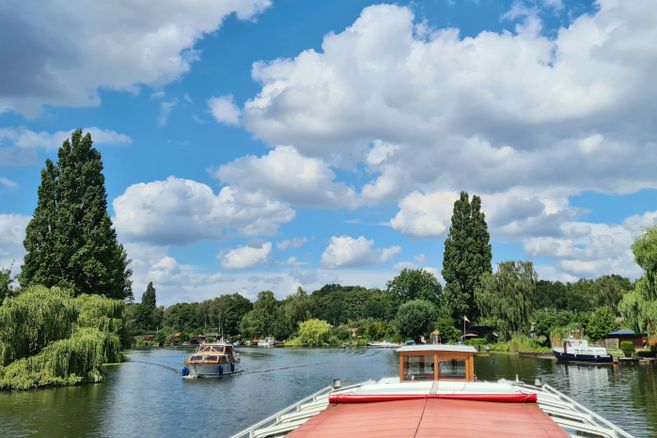 Eine traditionelle Barkasse mit rotem Faltdach fährt auf der Bille durch ein Gebiet mit idyllischen Kleingärten an beiden Ufern.