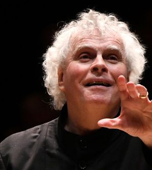 Ein Dirigent mit lockigem, weißem Haar dirigiert mit erhobener Hand.