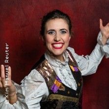 Eine lächelnde Frau in einem bunten Kostüm vor einem roten Hintergrund.