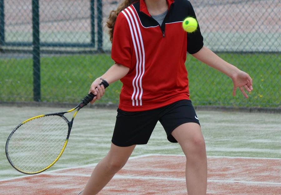 Ein Mädchen in rotem Sportshirt spielt Tennis auf einem Sandplatz.