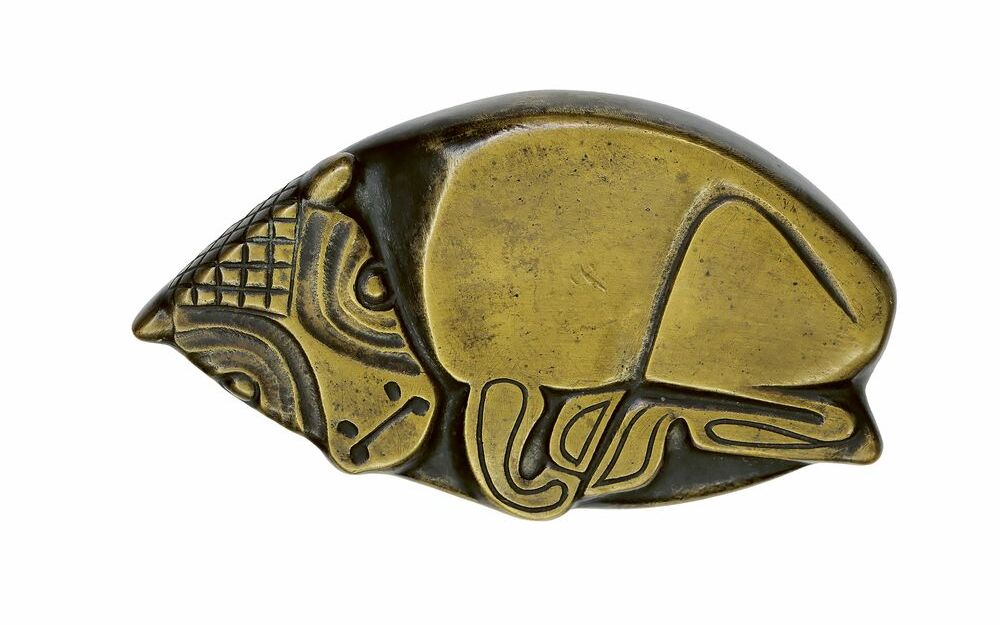 Foto einer Tierplastik. Zu sehen ist ein liegendes Kälbchen. Die metallische platte Plastik ist auf den erhobenen Flächen golden, die tieferliegenden Flächen sind schwarz.