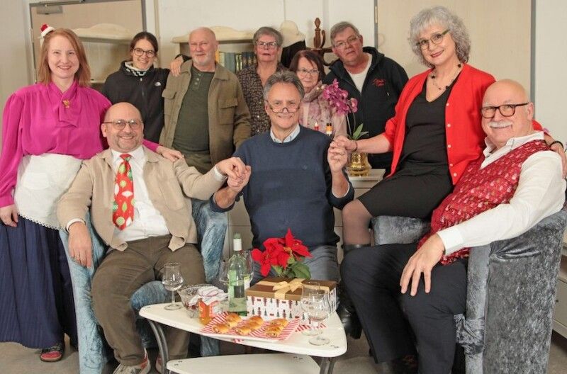 Eine Gruppe von Menschen sitzt und steht um einen Tisch mit Getränken und Snacks, lächelnd in die Kamera.