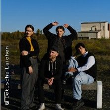 Vier Personen posieren auf einer Bank in einer ländlichen Umgebung mit einem Gebäude im Hintergrund.