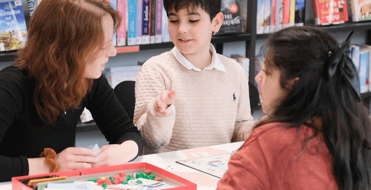 Drei Personen spielen ein Brettspiel in einer Bibliothek.