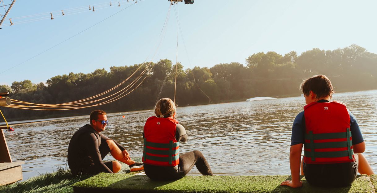 Drei Personen sitzen am Start der Wasserskianlage am Ostesee
