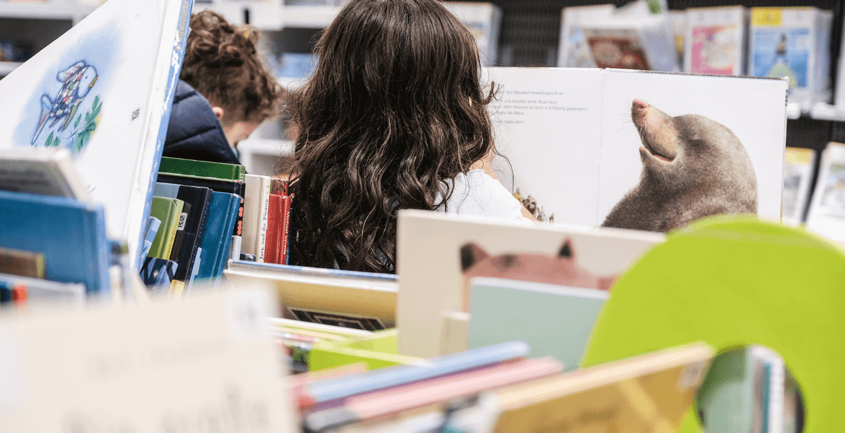 Zwei Kinder lesen in einer Bibliothek, umgeben von Kinderbüchern.