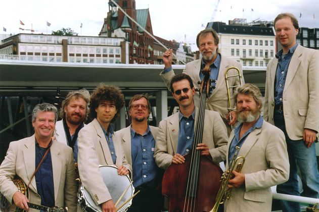 Eine Jazzband posiert mit Instrumenten vor einer städtischen Kulisse.