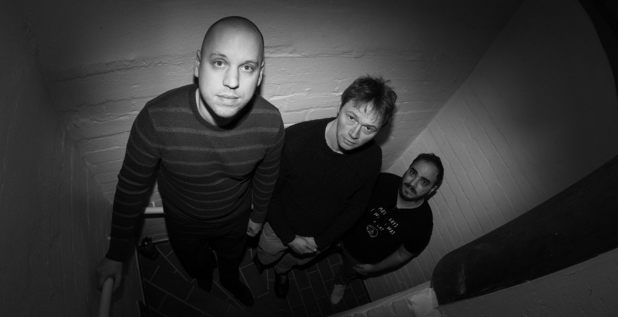 schwarz/weiß foto, drei Männer stehen in einem engen Treppenhaus von oben forografiert