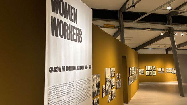 Ausstellung über Frauenarbeit in Glasgow und Edinburgh, 1850-1984, mit Fotos an gelben Wänden.
