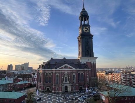 Blick auf die St. Michaelis Kirche in Hamburg bei Sonnenuntergang, mit der Elbphilharmonie im Hintergrund.