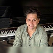 Ein Mann sitzt lächelnd vor einem Klavier.