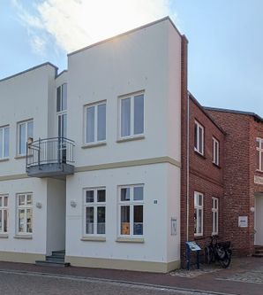 Ein modernes Gebäude mit weißer Fassade und Balkon neben einem älteren Backsteingebäude mit der Aufschrift 'Dithmarsia'.