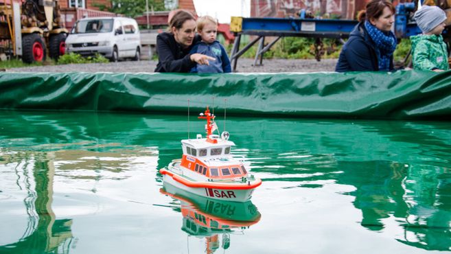 Ein Modellschiff schwimmt in einem Wasserbecken, während eine Frau und ein Kind es beobachten.