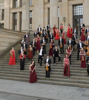 Eine Gruppe von Musikern in formeller Kleidung steht auf einer breiten Treppe vor einem historischen Gebäude.