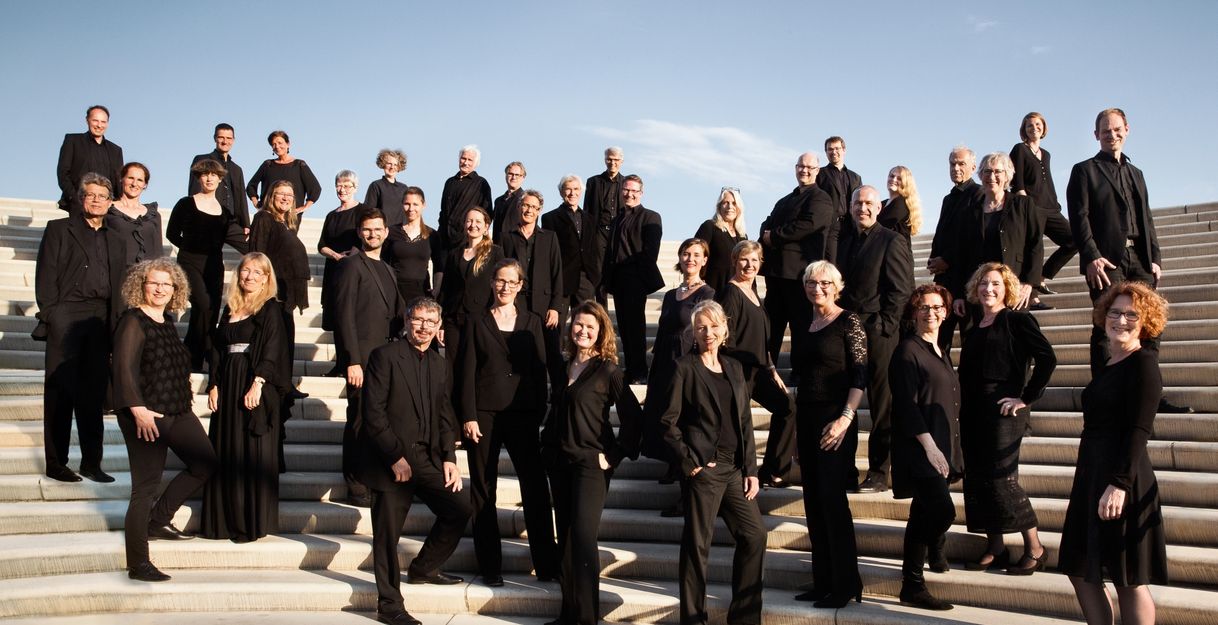 Eine Gruppe von Menschen in schwarzer Kleidung steht auf einer Treppe unter blauem Himmel.