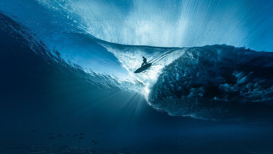 Ein Surfer reitet eine riesige, blau schimmernde Welle, die von unten beleuchtet wird.