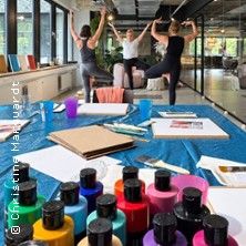 Gruppenevent Flow & Farbe: Drei Personen machen Yoga-Posen in einem hellen Raum mit großen Fenstern, davor liegen Malutensilien und bunte Farbtöpfe auf einem Tisch.