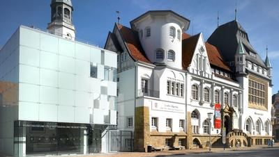 Modernes und historisches Gebäude nebeneinander mit Glasfassade und Türmen.