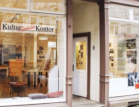 Eingang eines Kulturgeschichtsbüros mit großen Fenstern und einem Schild mit der Aufschrift 'KulturGeschichtsKontor'.