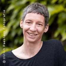 Porträt einer lächelnden Person mit kurzem Haar vor einem grünen Hintergrund.