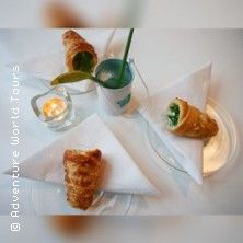 Drei gefüllte Blätterteighörnchen auf weißen Servietten, daneben eine Kerze und ein Getränk mit Strohhalm.