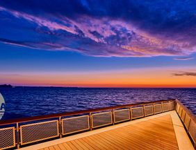 Eine Seebrücke erstreckt sich über das Meer bei Sonnenaufgang, mit einem farbenfrohen Himmel in Blau- und Orangetönen.