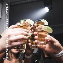 Menschen stoßen mit Tequila-Gläsern an, die mit Limettenscheiben garniert sind.