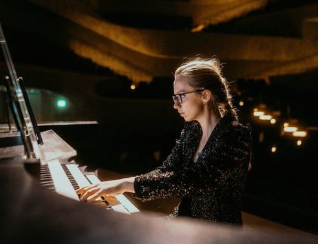Eine Frau spielt konzentriert Orgel in einem gedämpft beleuchteten Konzertsaal.