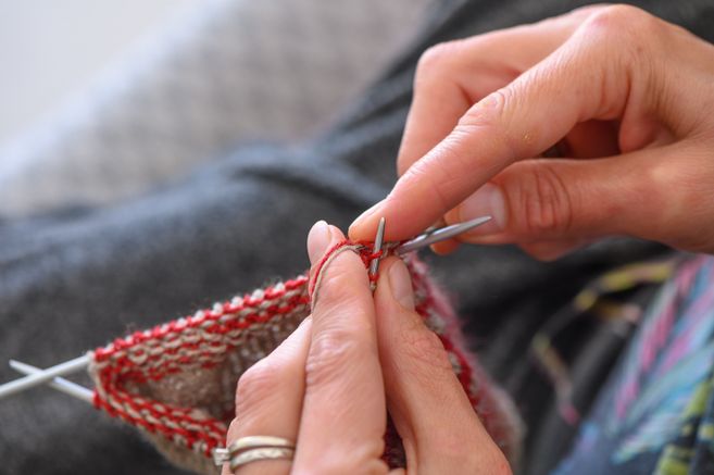 Nahaufnahme von Händen, die mit Stricknadeln und rotem Garn stricken.