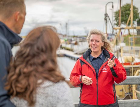 Eine Frau in roter Jacke spricht mit zwei Personen am Hafen von Büsum.
