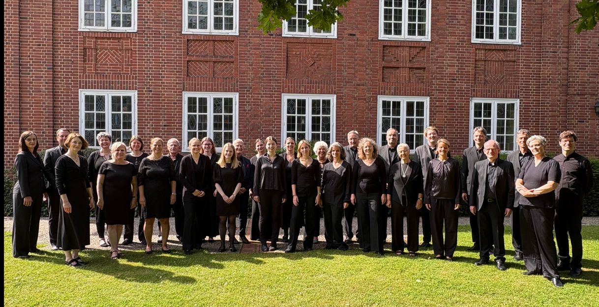 Eine Gruppe von Menschen in schwarzer Kleidung steht vor einem Backsteingebäude mit großen Fenstern.