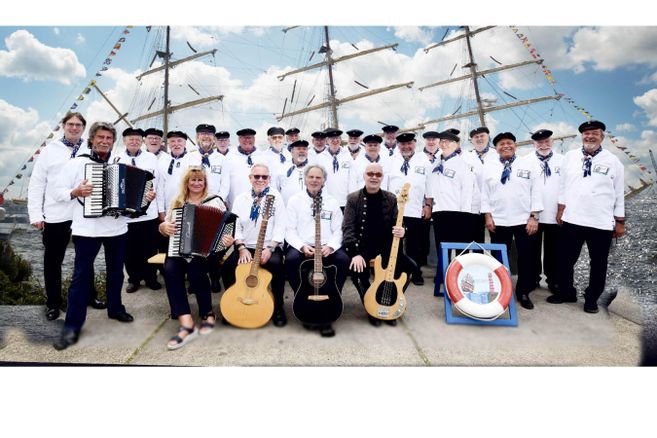 Eine Gruppe von Menschen in maritimer Kleidung posiert mit Musikinstrumenten vor einem Segelschiff.