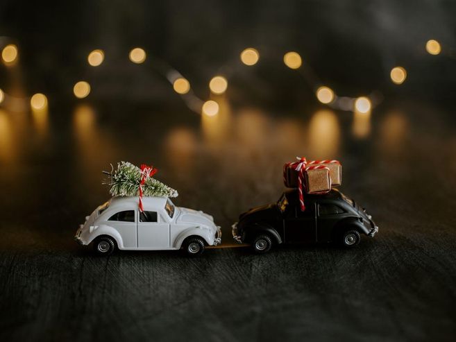 Zwei Spielzeugautos mit Weihnachtsbaum und Geschenken auf dem Dach vor unscharfen Lichtern.
