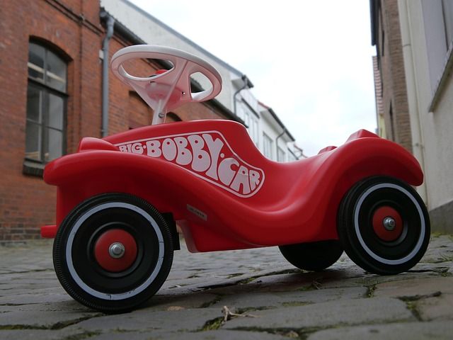 Ein rotes Bobbycar steht auf einem gepflasterten Weg zwischen Gebäuden.