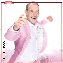 Ein Mann in einem rosa Anzug zeigt fröhlich auf den Betrachter.