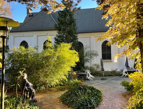 Ein ruhiger Garten mit Herbstlaub vor einer weißen Kirche mit gotischen Fenstern.